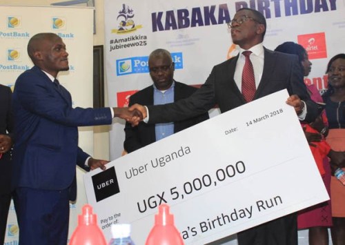 Aaron Tindie, country manager for Uber Uganda, hands a cheque to the Katikkiro of Buganda, Peter Mayiga